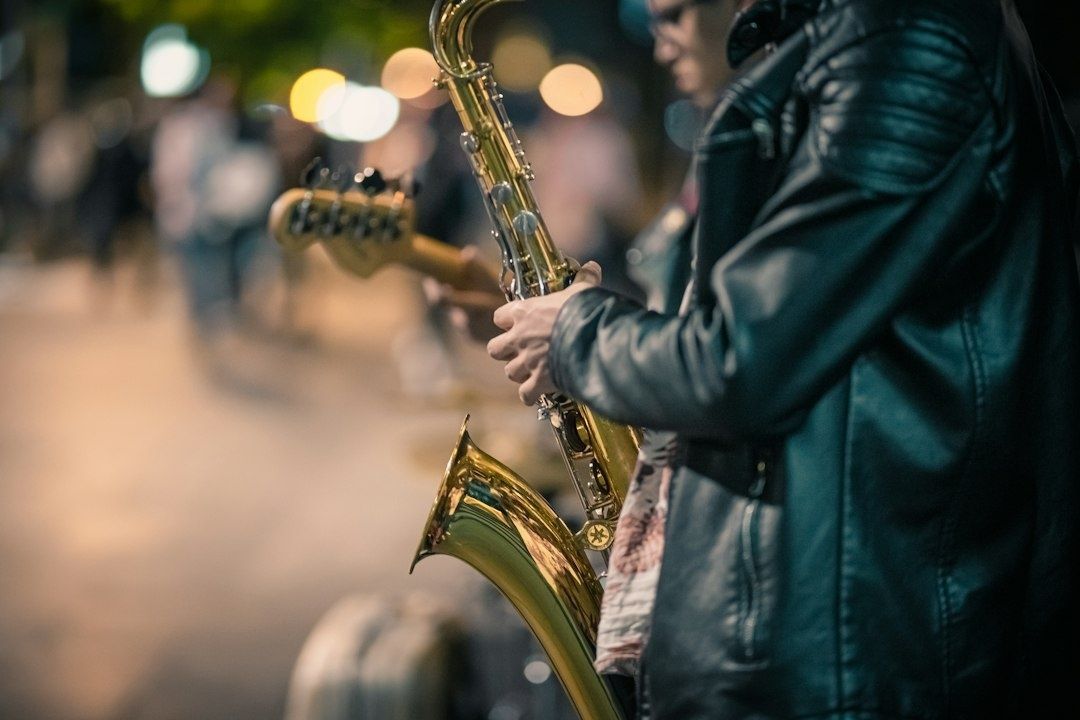 Saxofonist speelt buiten, met een gitarist op de achtergrond